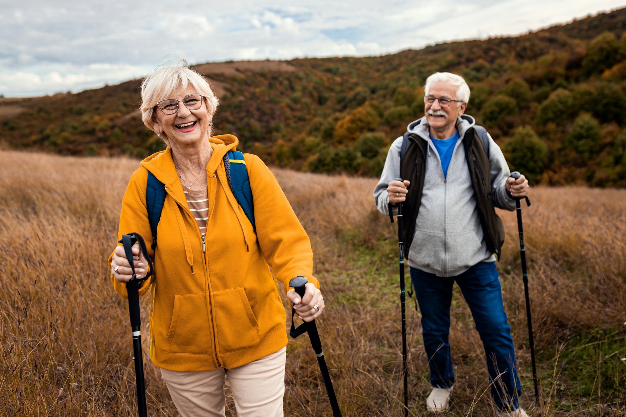 Active senior couple with backpacks hiking together in nature on autumn day.