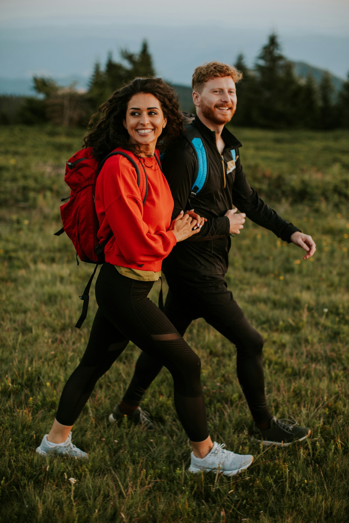 Smiling couple walking with backpacks over green hills